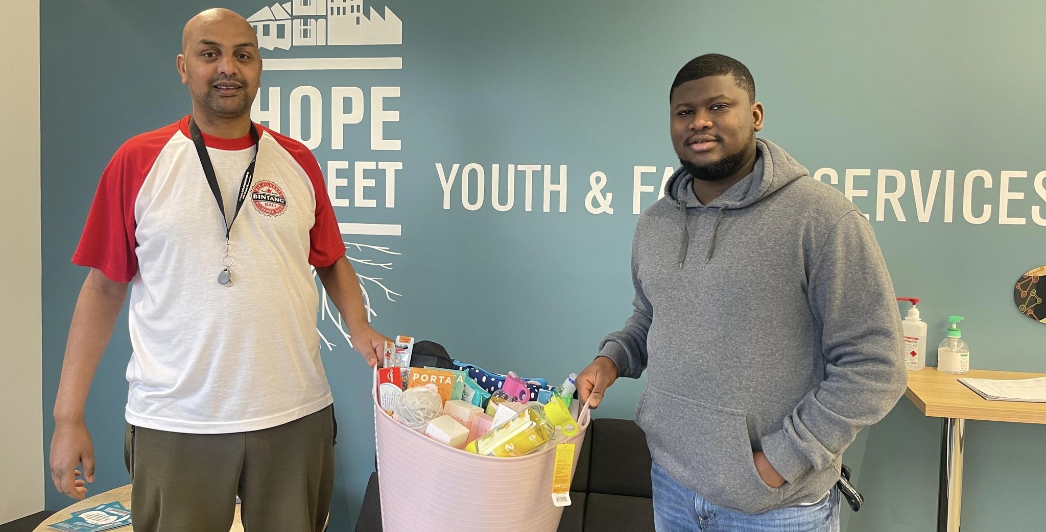 2 people from Hope Street Youth and Family Services holding a bucket of material aid